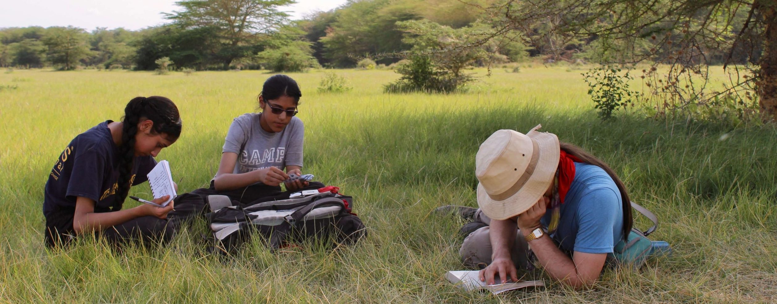 Travellers sitting on the grass reading and writing