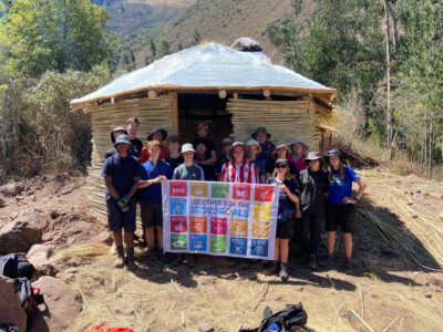UN SDG Flag held by Camps International Travellers in front of waterfall ticket booth project.