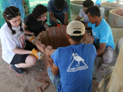 Group of students from the UAE on an expedition in Cambodia with Camps International. They're huddled together around a frame that will make a clay water storage pot
