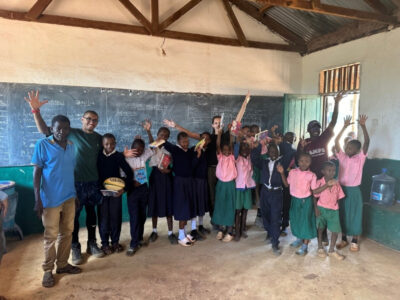 Group of African schoolchildren with new books, standing in a row in their classroom with their hands up. Students on an African Expedition with Camps International are joining in