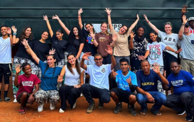 Group of students from the UAE on their expedition with Camps International in Kenya, Africa. They're all standing and kneeling in front of a safari truck, with their hands up in the air smiling.