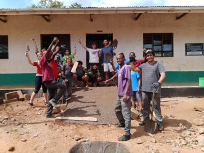 Group of students from the UAE with their hands up in the air, celebrating completing a new concrete ramp at a local school in Africa. This is part of their project work from their Camps International expedition.