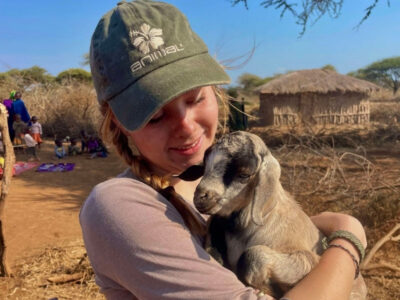 A young student on an Kenya Camps International expedition holding a baby goat after deworming it.