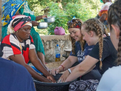 Two young female students on a Camps International trip in Africa learning to make chapatis with a local mama.