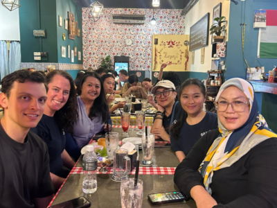 A group of teachers and Camps team members sat around a table eating dinner. They're all looking at the camera down the end of the table and smiling