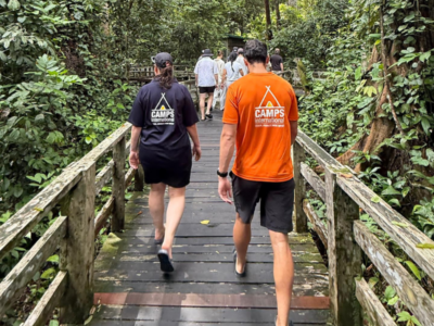 Two people walking across a wooden walkway wearing Camps International t-shirts