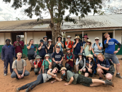 Group of students on a Camps International expedition to Kenya all standing together with some people laying in the foreground, posing for the camera