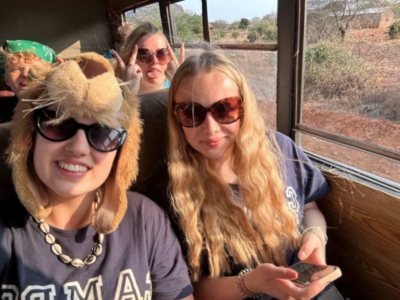 Group of girls on a bus in Kenya on a Camps International expedition in Kenya, with one of the girls wearing a lion hat