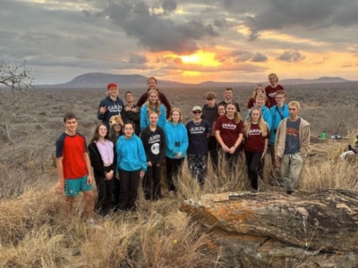 Group of students on a Camps International expedition to Kenya all standing together with a sunset behind them