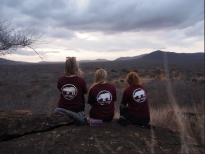 Group of three students on an expedition in Kenya overlooking the bush at Tsavo camp, all wearing Camp Kenya tshirts