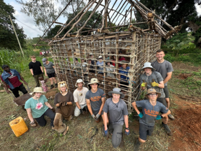 Group of student travellers standing in front of a house they are building in Kenya