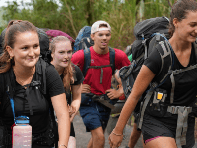 A group of three females and one male walking up a hill in full hiking gear, including large rucksacks and waterbottles. They are on a Raleigh International leadership expedition in Costa Rica and are undertaking the trek part of their journey.