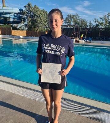 Teenage girl wearing Camps International t-shirt standing in from of a pool and smiling