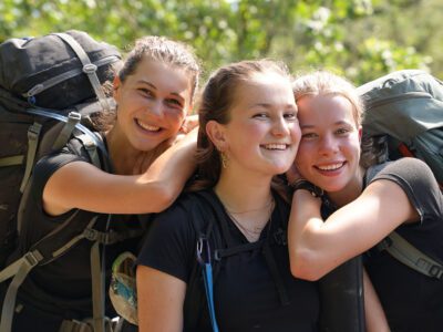 three girl travellers with backpacks hugging and smiling