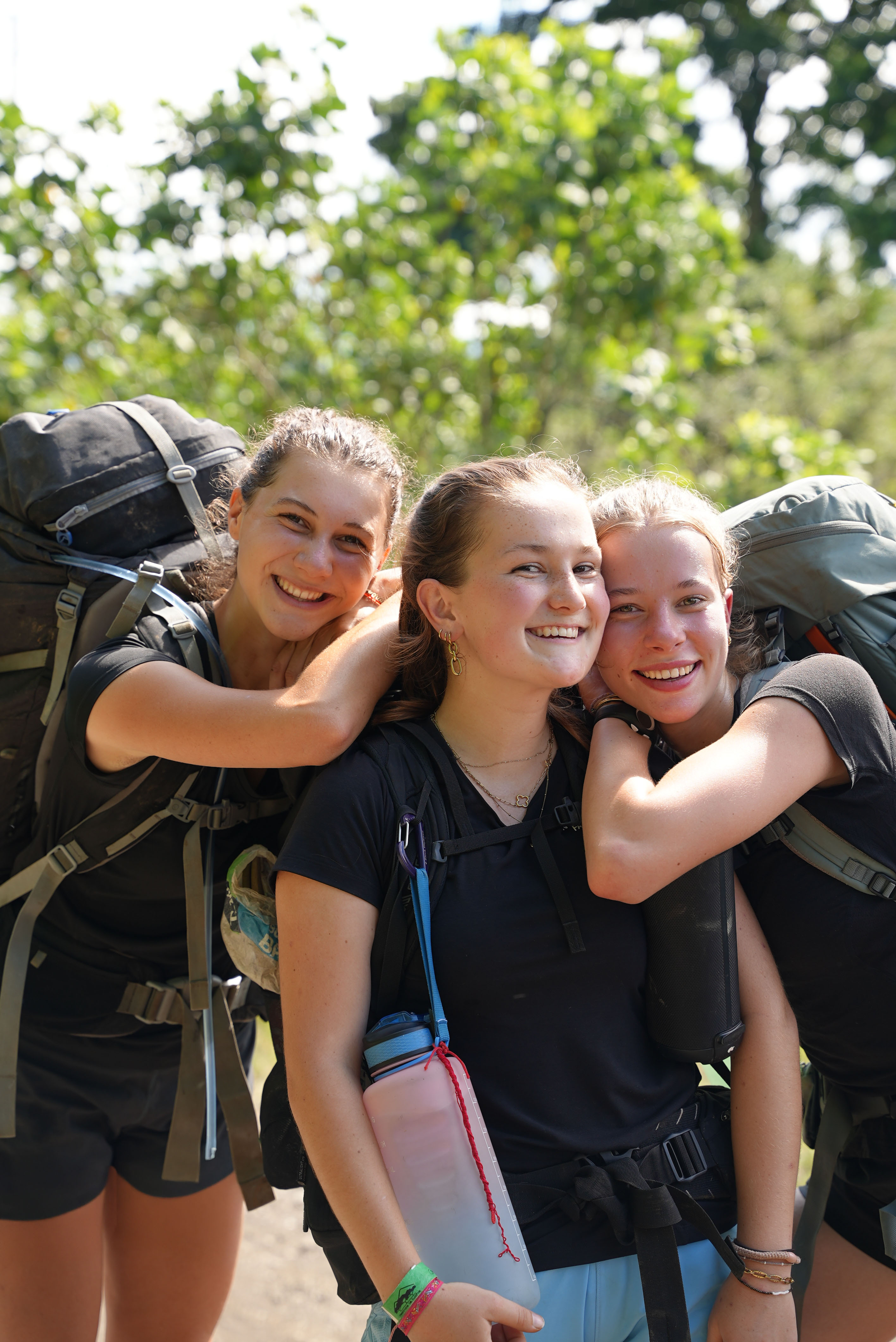 three girl travellers with backpacks hugging and smiling