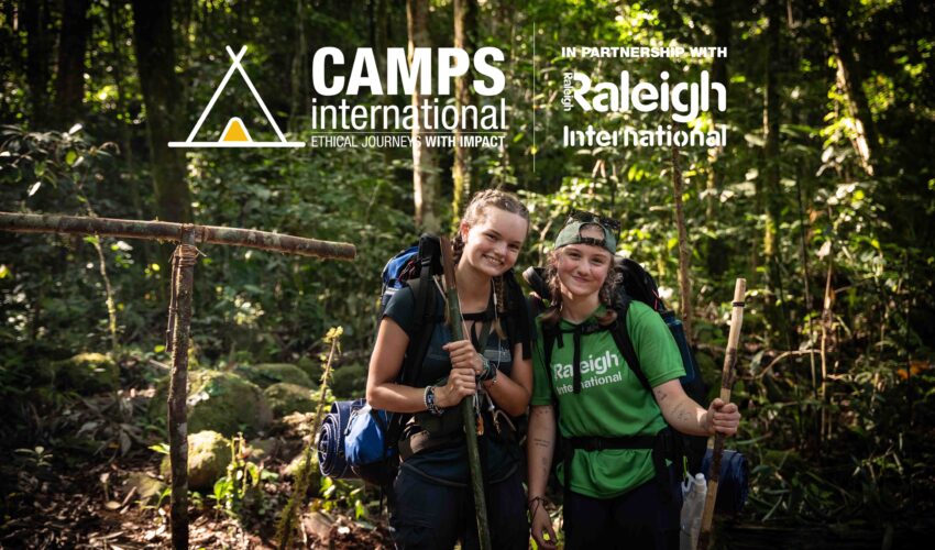 two girl travellers smiling and wearing backpacks on a trek