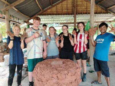 group of student travellers standing around a clay water pot they have been making