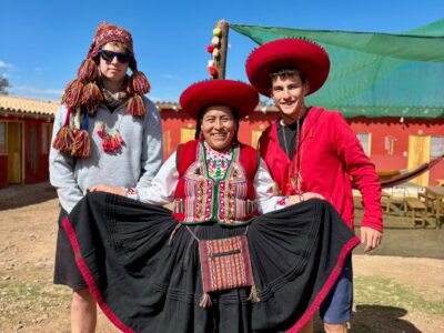 a local Peruvian woman dressed in traditional clothing standing next to two travellers wearing traditional hats and ponchos in Peru