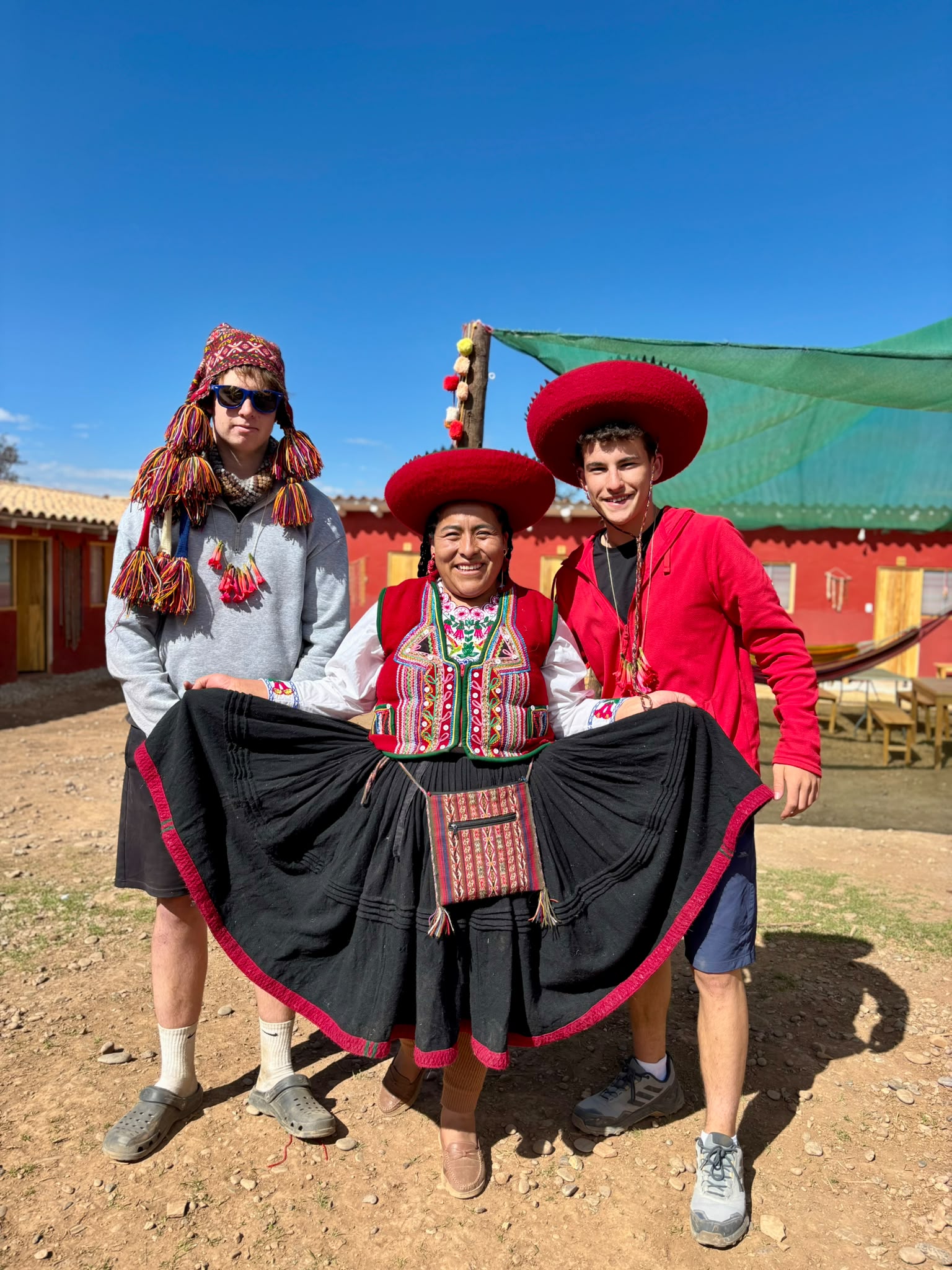 a local Peruvian woman dressed in traditional clothing standing next to two travellers wearing traditional hats and ponchos in Peru