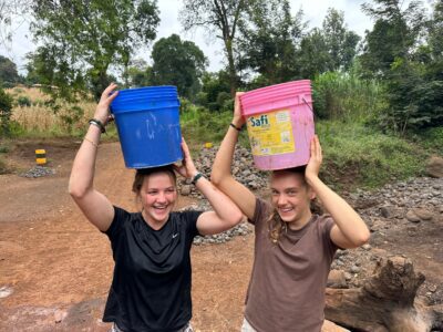 two girls carrying water buckets on their heads and smiling in Tanzania