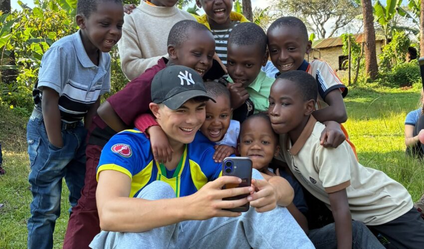 a student traveller showing something on his phone to local children in Tanzania